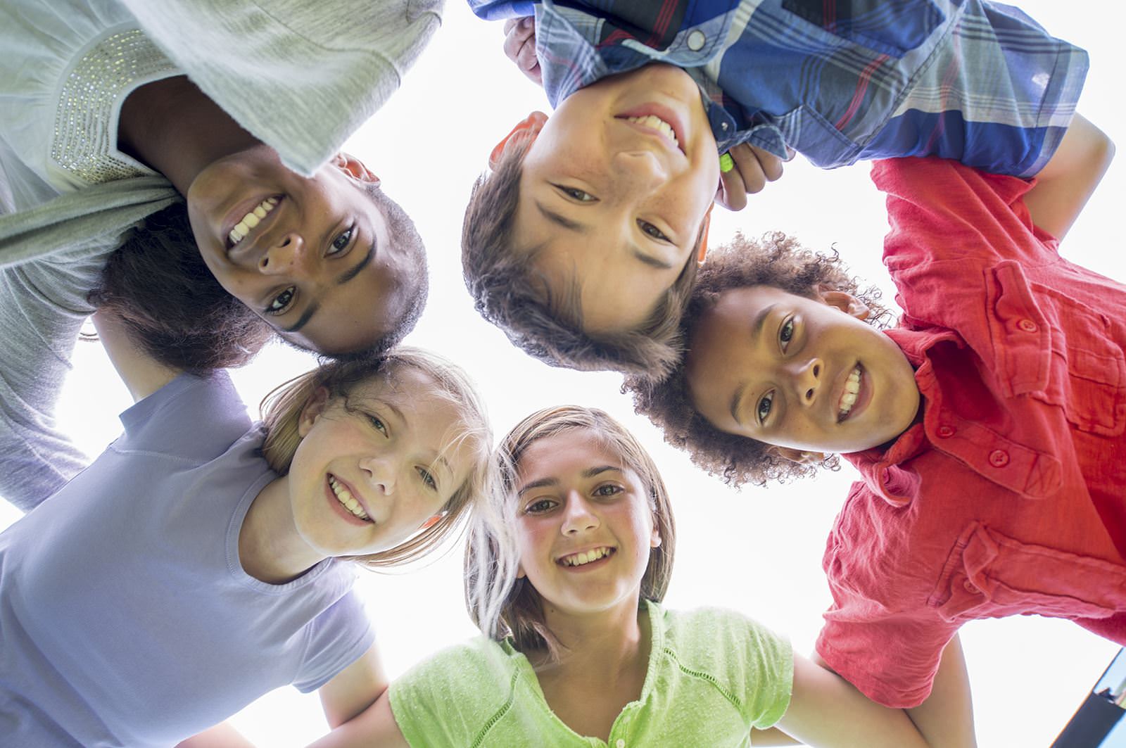 Five children with their heads together looking down at camera